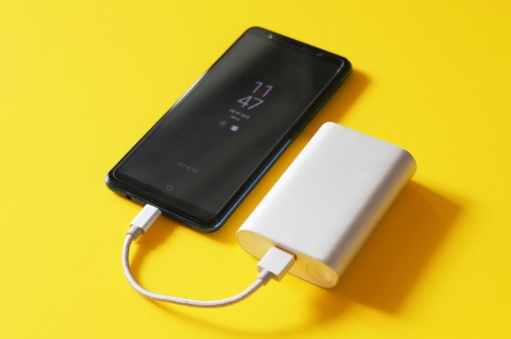 Kollasel pinnal telefon ja akupank ühendatud juhtmega.