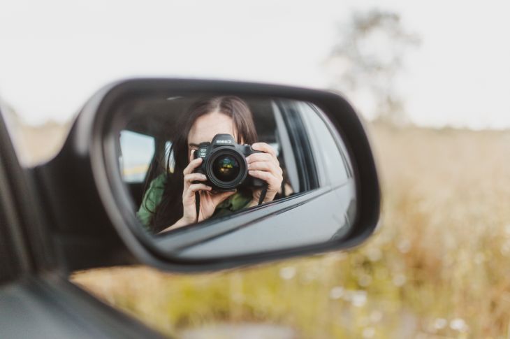 Naine teeb auto küljepeeglist pilti. Peeglist on näha naist, kelle näo varjab kaamera.