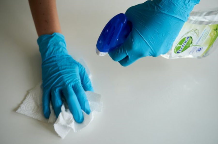 Hands with blue rubber gloves hold paper towels and detergent.