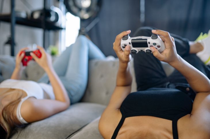 tüdrukud istuvad tagurpidi diivanil ja hoiavad käes PS4 pulte